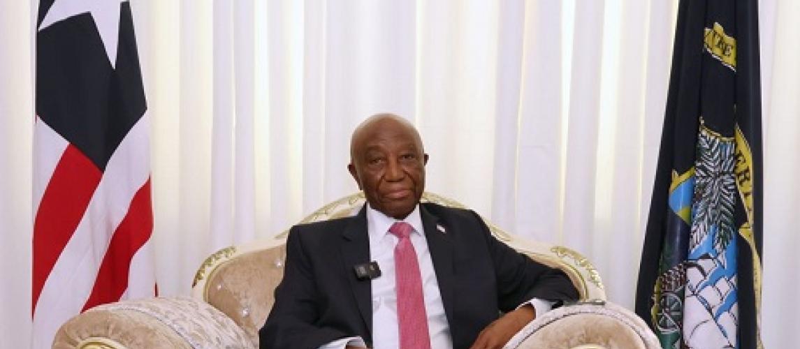 President Joseph Nyuma Boakai seated between the Liberian flag and the presidential standard